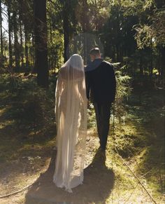 the bride and groom are walking through the woods on their wedding day, holding hands