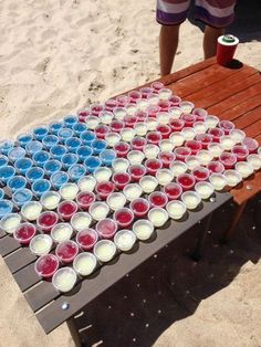 an american flag made out of cups sitting on top of a wooden bench in the sand