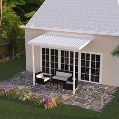 a patio with chairs and tables next to a white house in the grass, surrounded by flowers