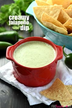 a red pot filled with dip surrounded by tortilla chips and jalapenos