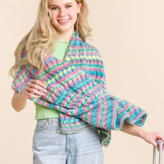 a woman holding a suitcase and wearing a multicolored knitted shawl over her shoulders