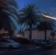 a blurry photo of cars driving down the street at night time with palm trees in front of them