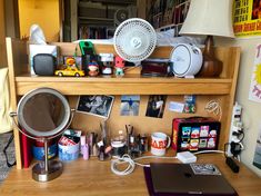 a cluttered desk with various items on it and a fan above the top shelf