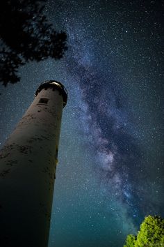 the night sky is filled with stars above a light house and trees, as seen from below