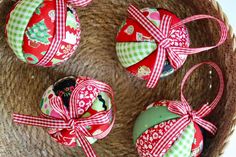 four ornaments are wrapped in red and green ribbons on a woven basket with ribbon around them