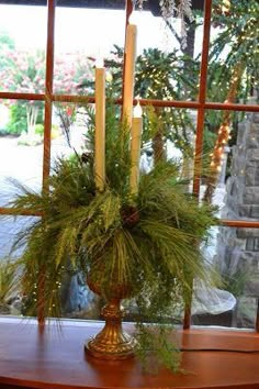 a wooden table topped with a vase filled with pine cones and greenery next to a window