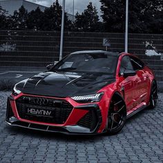 a red and black sports car parked in front of a fence