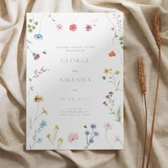 a wedding card with wildflowers and grass on it sitting on top of a bed