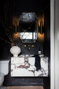 a black and white bathroom with marble counter top, gold mirror above the sink and toilet