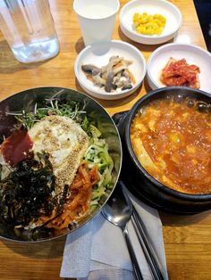 a wooden table topped with bowls filled with different types of food and utensils