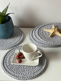 two crocheted placemats on a table with a cup and saucer