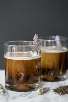 two glasses filled with liquid sitting on top of a table next to lavenders and herbs