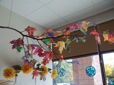 a branch with leaves and sunflowers hanging from it's branches in front of a window