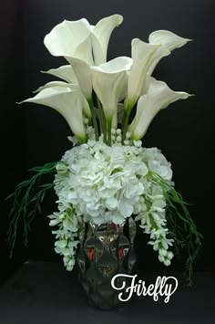 there is a vase with white flowers and greenery in it on the black background