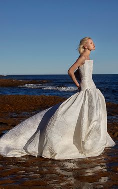 a woman in a wedding dress standing on the beach