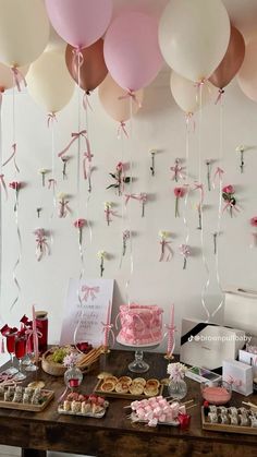 a table topped with lots of pink and white balloons hanging from the ceiling above it