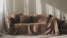 a couch covered in a brown blanket next to a table with a lamp on it