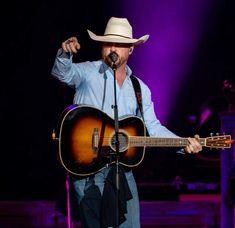 a man in a cowboy hat singing into a microphone and playing an acoustic guitar on stage