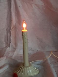 a lit candle on a white cloth with a red cord in the foreground and a pink background