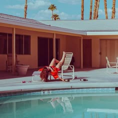 a woman laying on top of a chair next to a swimming pool with palm trees in the background