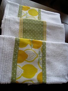 three white towels with yellow and green designs on them sitting on a wooden table in front of a window