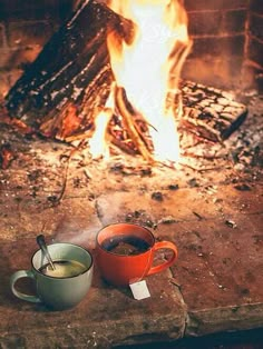 two cups of coffee sitting in front of a fire