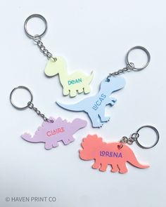 three dinosaur shaped key chains with name tags attached to them, on a white background