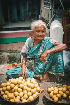 an old woman sitting on the ground next to baskets of potatoes in front of her