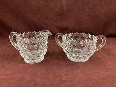 two glass pitchers sitting on top of a brown cloth