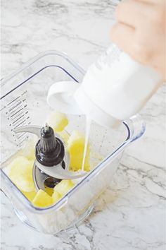 someone is pouring something into a blender filled with yellow and black fruit, including pineapples