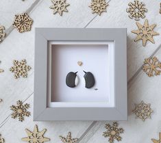 two black and white earrings are in a shadow box with snowflakes around them