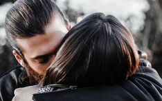 a man and woman embracing each other in front of trees