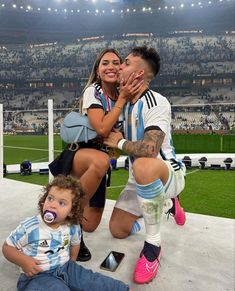 a man, woman and child sitting on the ground in front of a soccer stadium