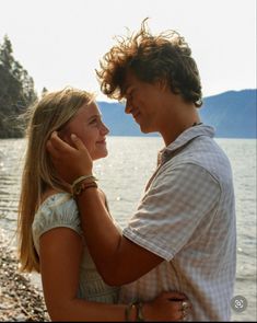 a young man and woman standing next to each other near the water's edge