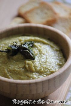 a wooden bowl filled with green dip next to crackers