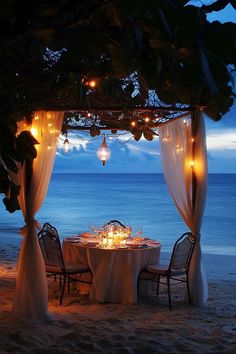 an outdoor dining set up on the beach at night with candles lit in front of it