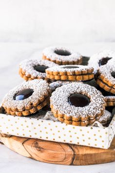 powdered sugar covered donuts sitting on top of a wooden platter with jam in the middle