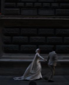 a bride and groom walking down the street in front of a stone building at night