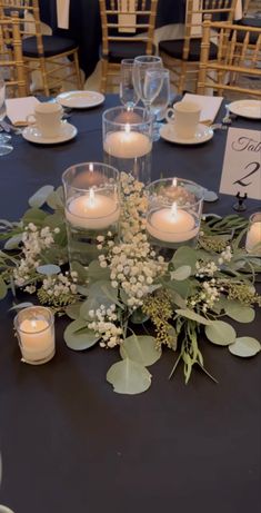 the table is set with candles and greenery for an elegant centerpieces display