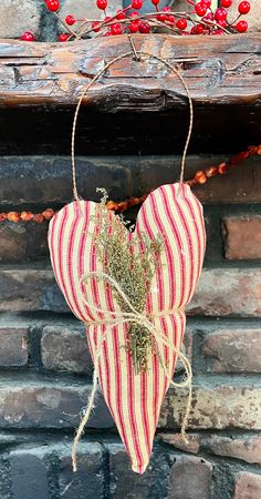 a red and white striped heart hanging from a brick wall with berries on the mantle