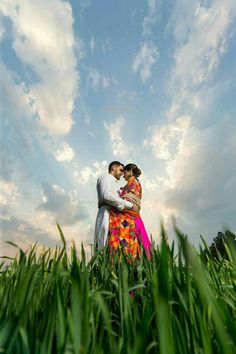 a man and woman standing in tall grass under a cloudy sky