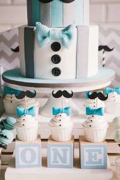 a blue and white cake with mustaches on it's top, surrounded by little cupcakes