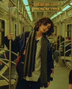 a person standing on a subway train with a scarf around their neck and looking at the camera