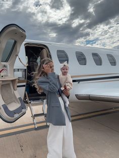 a woman holding a baby standing in front of a private jet on the tarmac