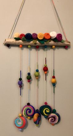 an art piece made out of felt and yarns hanging from a wooden stick on the wall