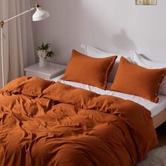 a bed with orange sheets and pillows in a white room next to a lamp on a table