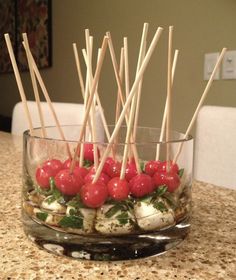 a glass bowl filled with tomatoes and skewers on top of a marble counter