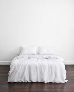 a bed with white sheets and pillows on top of it in a room that has hardwood floors