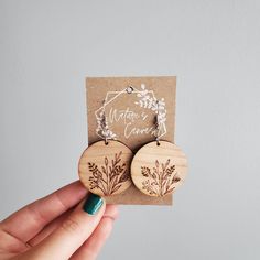 a hand holding two wooden earrings with floral designs on the front and back of them