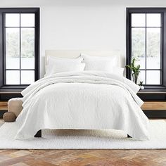 a bed with white linens and pillows in front of two large black framed windows